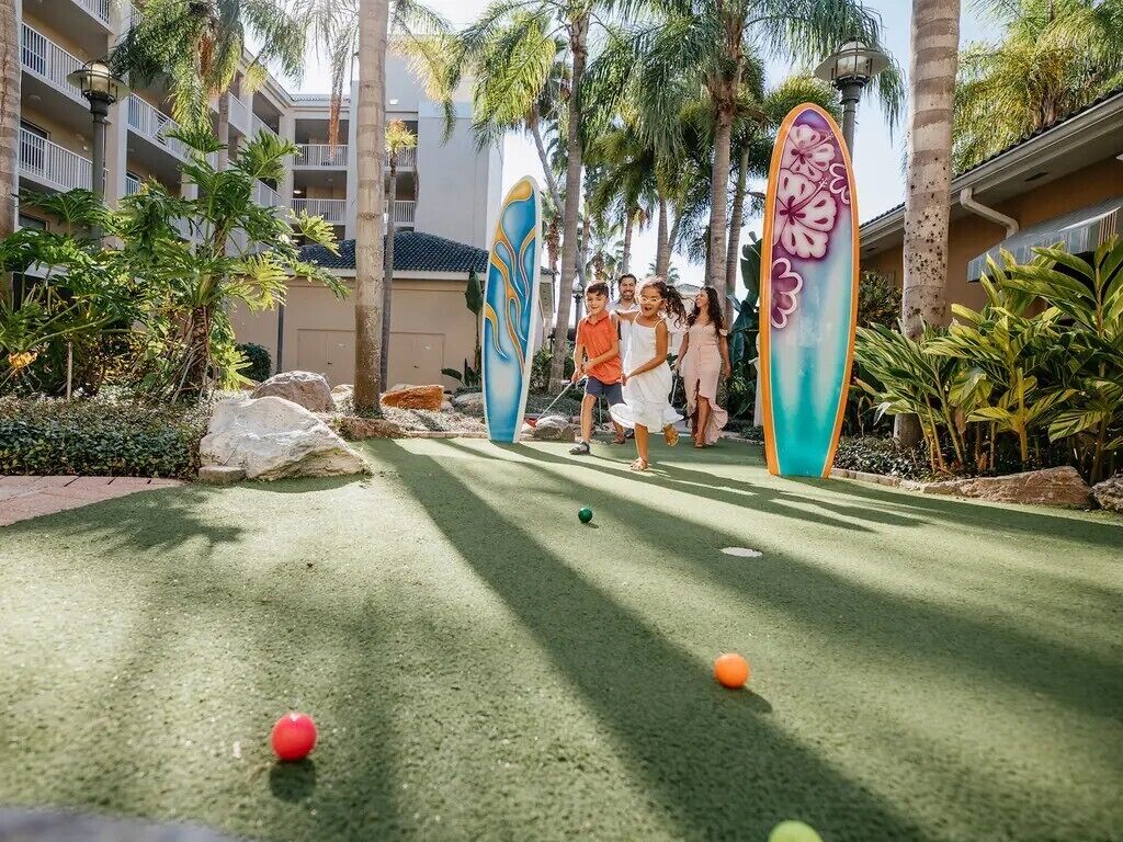 A courtyard with a miniature golf course, palm trees, and a building with balconies.