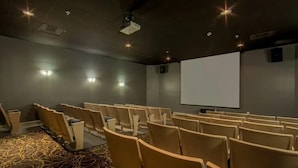 Une salle de conférence avec des rangées de chaises, un écran de projection et une moquette à motifs clairs.