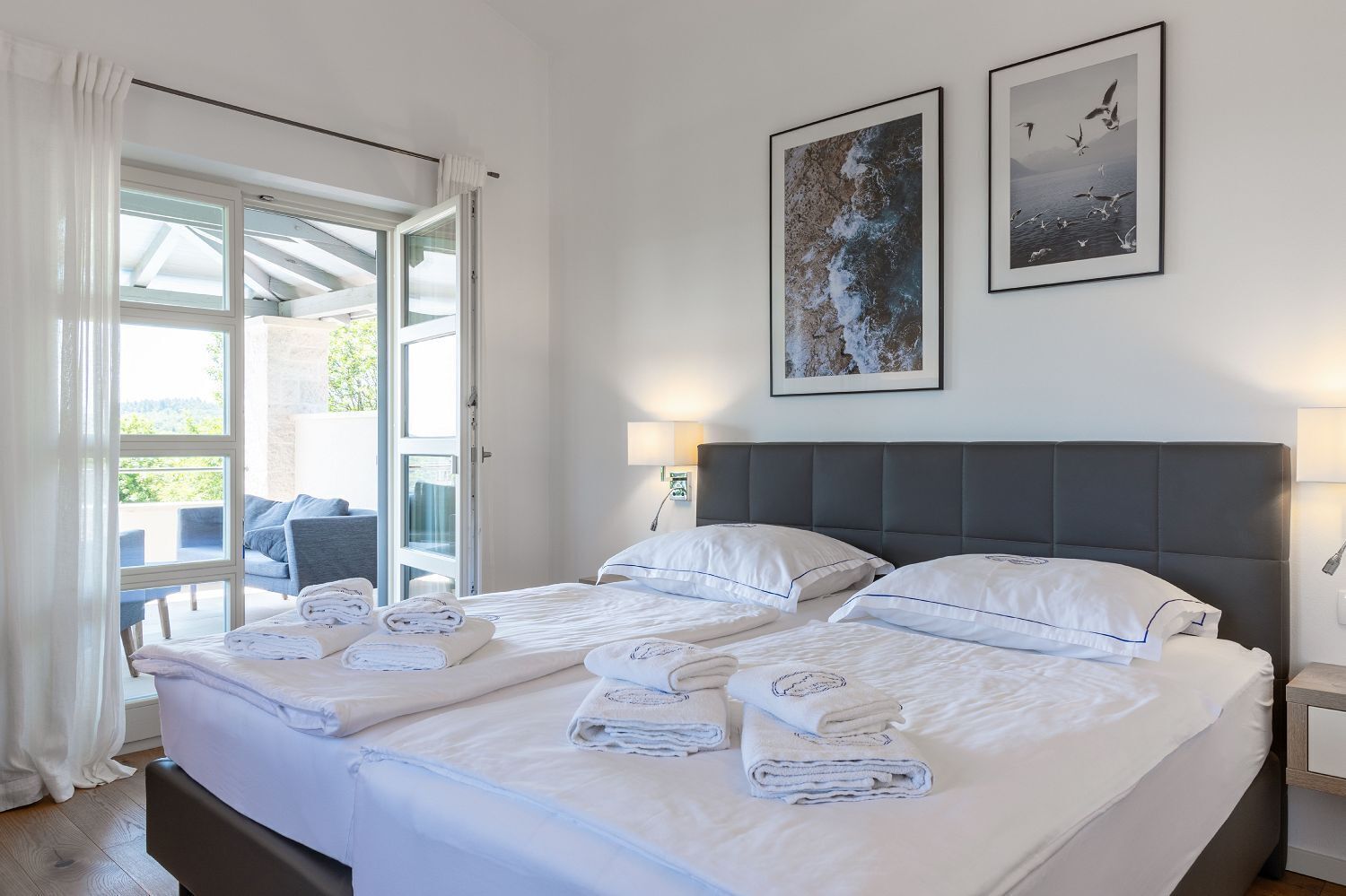 A hotel room with a large bed, two side-by-side beds, a balcony with outdoor seating, and two framed pictures on the wall.