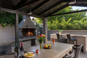 Un patio exterior con una parrilla, una mesa de comedor, sillas y una variedad de comida y bebidas.