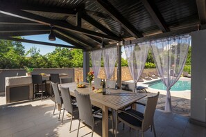 Un patio exterior con mesa y sillas, una parrilla y vista a una piscina.
