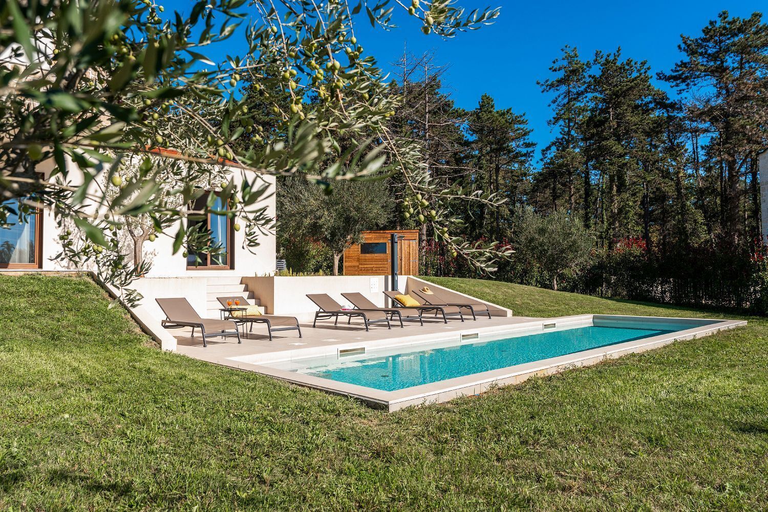Uma área de piscina moderna ao ar livre, com espreguiçadeiras e uma pequena estrutura de madeira.