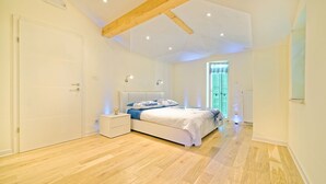 Ein Schlafzimmer mit Holzboden, einem Bett mit weißer Bettwäsche, einem Nachttisch und einem Fenster mit Jalousien.