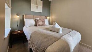 Een netjes ingerichte slaapkamer met een bed, nachtkastje, wanddecoratie en een bedlamp.