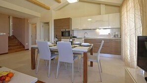 Una cucina moderna con mobili bianchi, un'area pranzo con tavolo apparecchiato per quattro persone e una TV su un mobile basso.