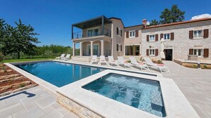 Una casa moderna de dos pisos con piscina, mobiliario exterior y fachada de piedra.