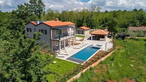 Una casa moderna de dos pisos con piscina, rodeada de exuberante vegetación y árboles.