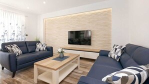 Una sala de estar moderna con dos sofás oscuros, una mesa de centro de madera y un televisor de pantalla plana montado en una pared con textura.