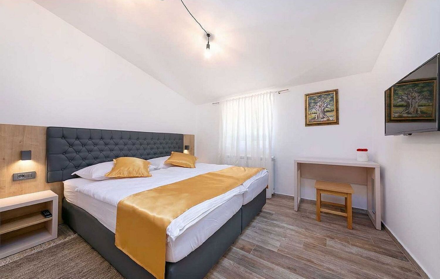 A modern bedroom with a large bed, bedside tables, a desk, and artwork on the walls.