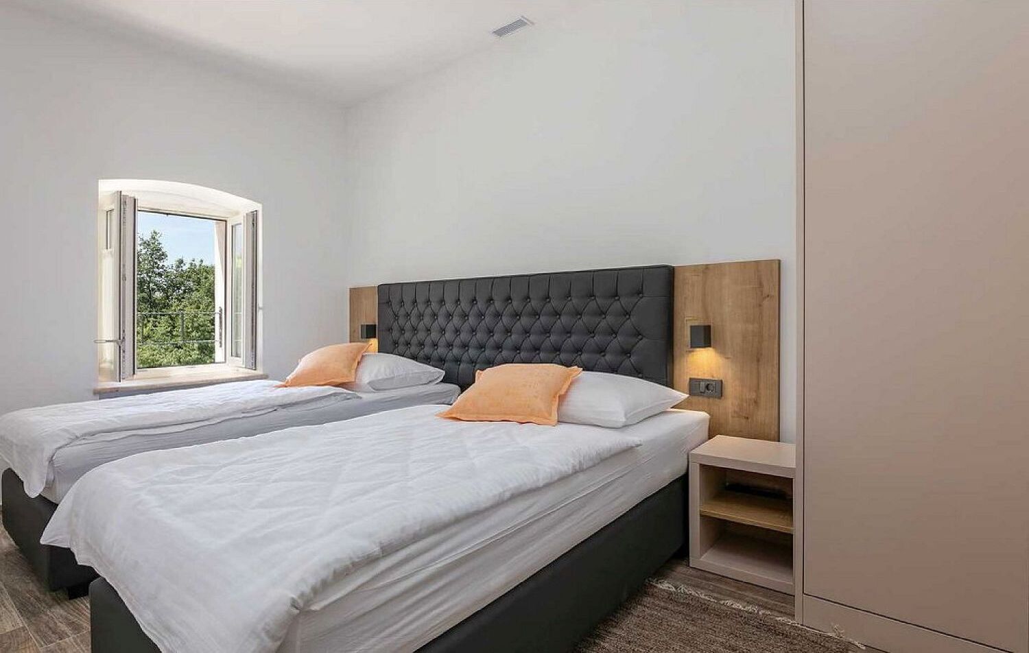 A double bed room with a large window, a dark headboard, and bedside lamps.