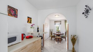 Una cucina compatta con forno a microonde, bollitore rosso e un piccolo elettrodomestico rosso. Si intravede, attraverso un arco, un'area pranzo con un tavolo rotondo e sedie.