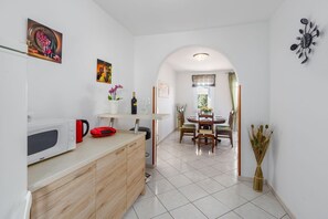 A compact kitchen with a microwave, red kettle, and a small red appliance. A dining area with a round table and chairs is visible through an archway. - Dog-friendly holiday home just 700 metres from the beach with barbecue and washing machine (Porec)
