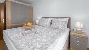 Un letto rifatto con una coperta a fiori, un comodino con una lampada e un portaoggetti in legno con cassetti.