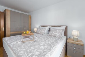 A neatly made bed with a floral bedspread, a bedside table with a lamp, and a wooden nightstand with drawers. - Dog-friendly holiday home just 700 metres from the beach with barbecue and washing machine (Porec)
