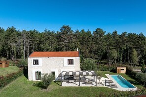 Ein zweistöckiges Steinhaus mit rotem Ziegeldach, einem Swimmingpool und einer Terrasse mit Gartenmöbeln.