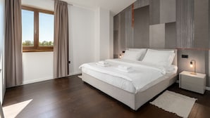 A modern bedroom with a large bed, a nightstand with a lamp, and a view of the outdoors through a window with curtains. - Special stone house with private pool, panoramic view, garden, barbecue, washing machine (Višnjan)