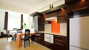 Eine moderne Küche mit dunklen Schränken, einem weißen Kühlschrank und einem Essbereich mit Tisch und Stühlen.