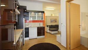 Eine moderne Küche mit Geschirrspüler, ein Essbereich mit Tisch und Stühlen, ein Sofa und eine Holztür.