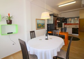 A dining area with a round table, chairs, a hanging light fixture, a potted plant, and a painting on the wall. - Idyllic apartment with children's playground in front of the building and only 700 metres from the beach (Porec)
