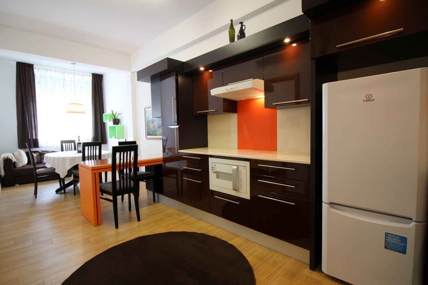 Une cuisine moderne avec des meubles de couleur sombre, un réfrigérateur blanc et un coin repas comprenant une table et des chaises.