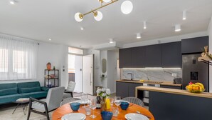 Una sala de estar moderna con un sofá, una mesa de comedor lista para cuatro personas y una cocina con armarios oscuros y un salpicadero de mármol.
