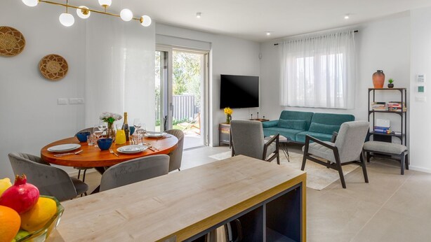 Una sala de estar moderna con un sofá verde azulado, un comedor con mesa de madera y un televisor montado en la pared.