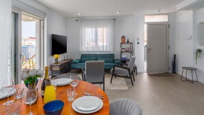 Una sala de estar moderna con un sofá, un televisor y un comedor con una mesa dispuesta para dos personas.