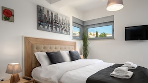 A modern hotel room with a large bed, a flat-screen TV, a cityscape painting, and a window with a view of buildings. - Luxury apartment with sea view, only 50 metres from the marina and 300 metres from the beach (Vrsar)
