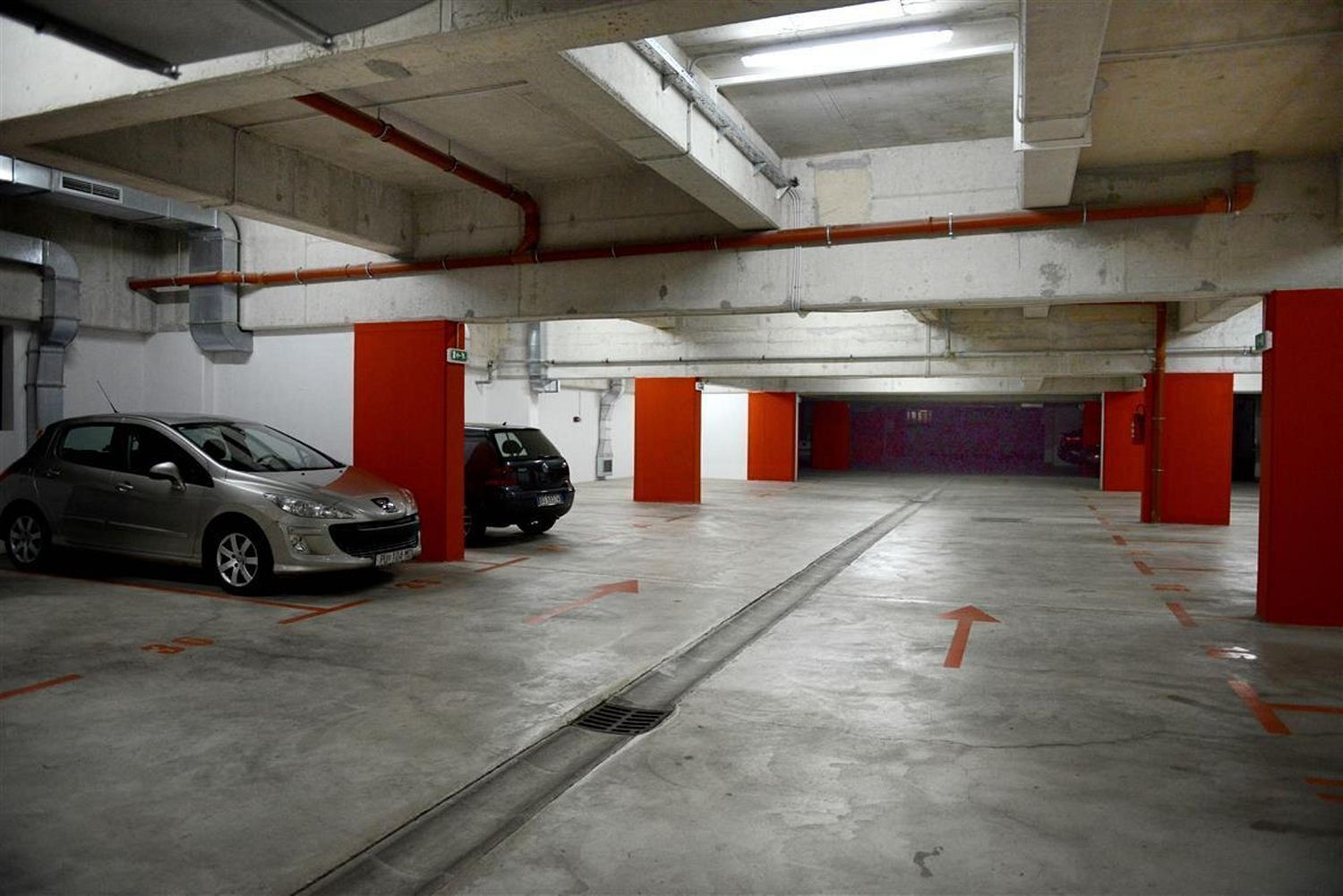 En parkeringskælder med beton gulve og røde søjler.