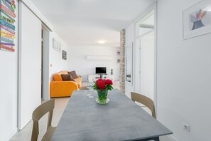 A modern living room with a grey dining table, orange sofa, and a TV. - Extravagant apartment in a perfect location – 300 metres from the beach and 100 metres from the centre (Porec)