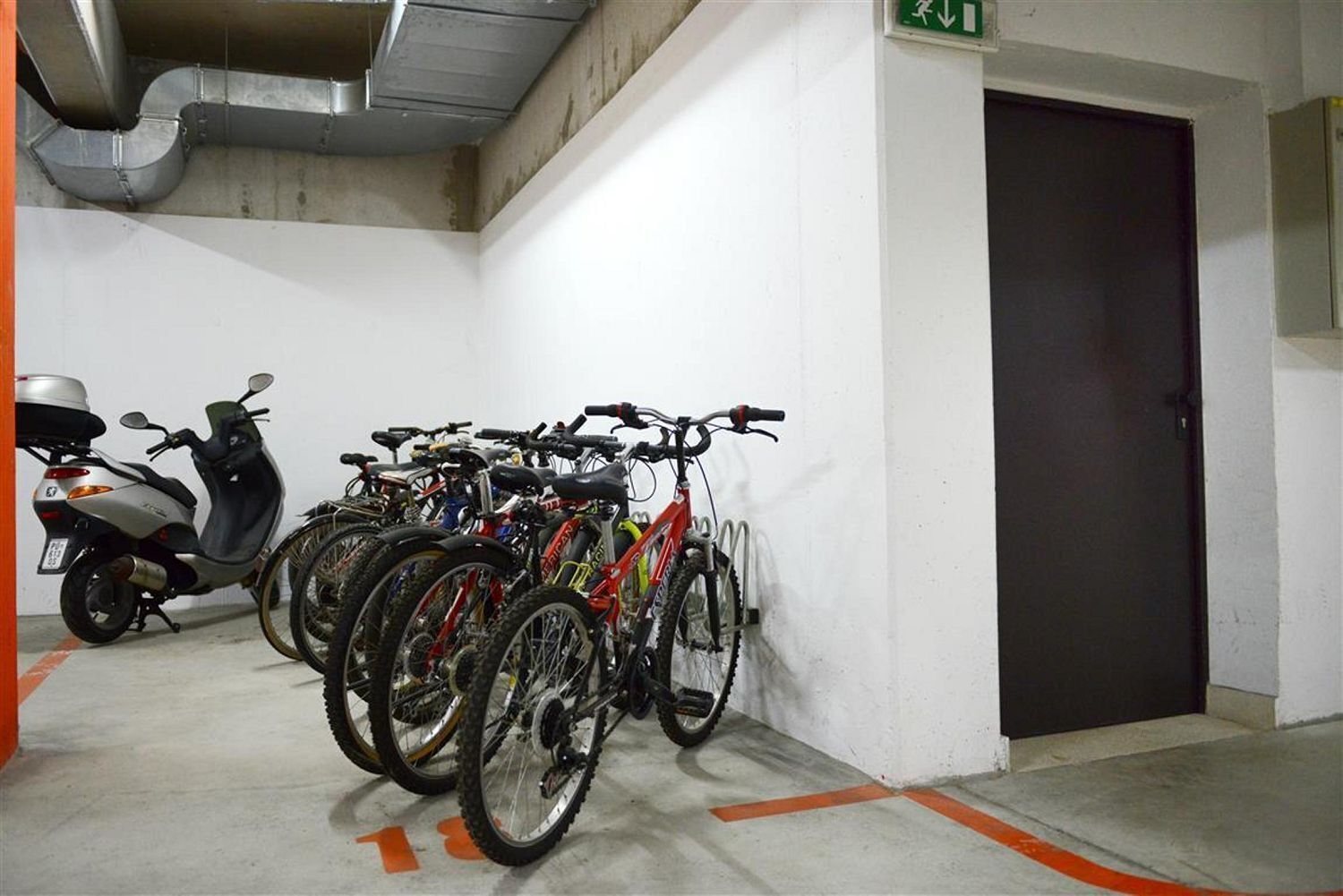 A parking garage with multiple bicycles and a scooter parked against the wall.