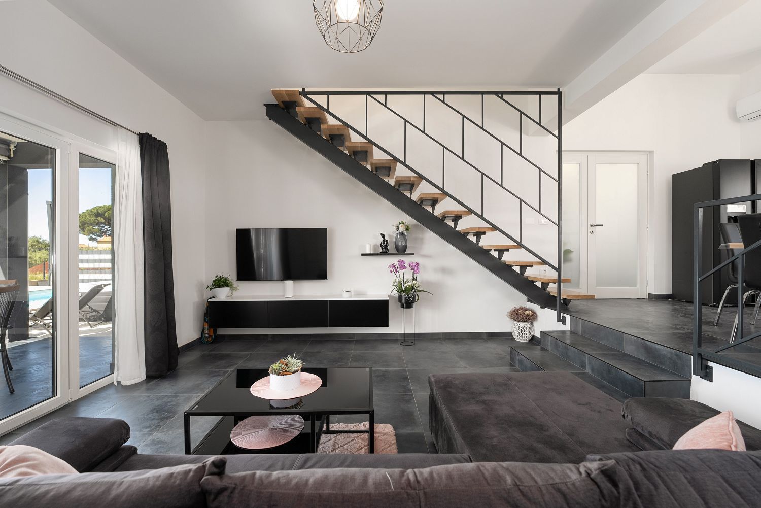 A modern living room with a staircase, a flat-screen TV, a coffee table, and a sofa.