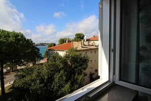 A view from a window overlooking a coastal area with buildings and trees. - Charming apartment right on the promenade of Porec with sea view (Porec)
