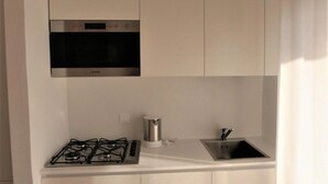 A compact kitchen with white cabinetry, a stainless steel range hood, a gas stove, a kettle, and a sink. - Comfortable Apartment in Jesolo (Jesolo)