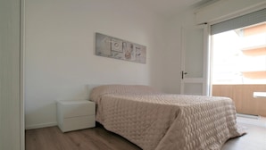 A bedroom with a bed, a nightstand, a wall art piece, and a sliding glass door to a balcony. - Comfortable Apartment in Jesolo (Jesolo)
