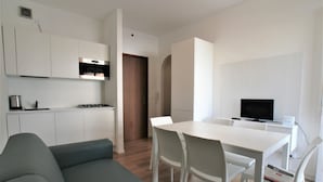 A modern kitchen with white cabinets, a built-in oven, and a dining area with a white table and chairs. - Comfortable Apartment in Jesolo (Jesolo)