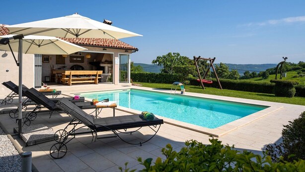 Un espace aménagé au bord de la piscine, avec des chaises longues, un coin salon abrité et une vue sur le paysage.