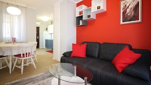 A modern living room with a black sofa, red cushions, a glass coffee table, and white dining chairs. - Idyllic apartment just 700 metres from the beach with balcony, garden and WiFi (Porec)