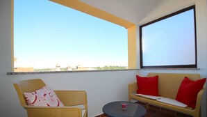 A balcony with wicker furniture, a small table, and a large window offering a view of buildings and greenery. - Idyllic apartment just 700 metres from the beach with balcony, garden and WiFi (Porec)