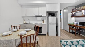 Una cucina moderna con mobili bianchi, un forno a microonde integrato e un frigorifero. È presente un tavolo da pranzo apparecchiato con piatti e un portatile su una scrivania in legno.