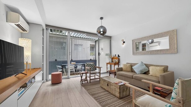 Un soggiorno moderno con TV, divano e tavolino. C'è una zona pranzo con sedie e tavolo. La stanza ha un'ampia finestra e una luce a soffitto.