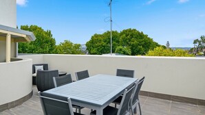 Una terrazza sul tetto con tavolo e sedie, un'antenna parabolica e vista su alberi ed edifici.