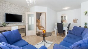 A modern living room with a flat-screen TV, a dining area with a table and chairs, and a staircase leading to another level. - Picturesque, dog-friendly holiday home just 400 metres from the beach with BBQ, cot (Porec)