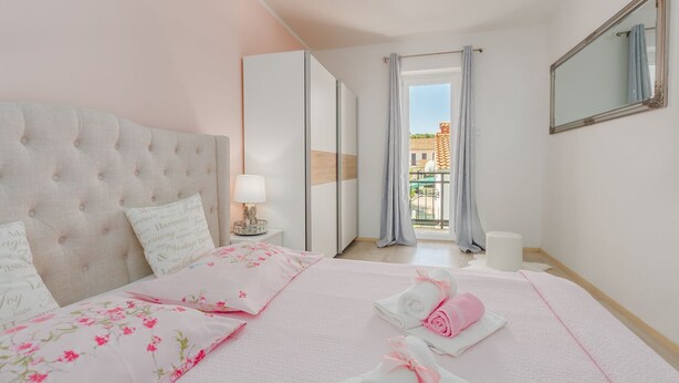 A bedroom with a tufted headboard, a bed with floral bedding, a bedside lamp, and a view of a balcony through a window with curtains. - Picturesque, dog-friendly holiday home just 400 metres from the beach with BBQ, cot (Porec)