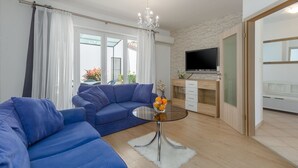 A modern living room with a blue sofa, a glass coffee table with fruit, a TV on a wooden cabinet, and a stone wall. - Picturesque, dog-friendly holiday home just 400 metres from the beach with BBQ, cot (Porec)
