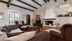 Una sala de estar con pared de piedra, chimenea, televisor y un conjunto de sofás.