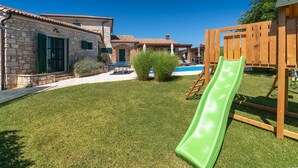 Un patio trasero con un tobogán verde, un edificio de piedra y una piscina.