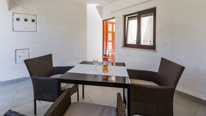 Una habitación pequeña y luminosa con una mesa y dos sillas de mimbre, una botella de vino y una copa sobre la mesa.