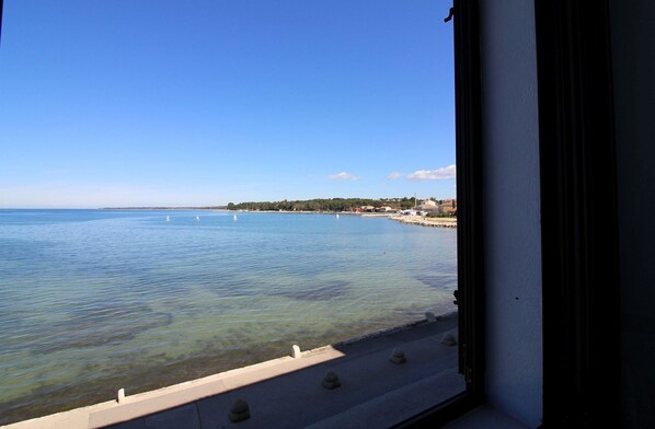 A coastal view from a window overlooking a calm sea with sailboats, a sandy beach, and a distant shoreline with buildings. - Fantastic location in the centre of Porec, only 200 metres from the beach with sea views (Porec)