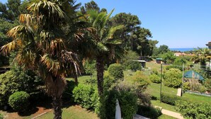 A lush garden with palm trees and various shrubs, a pathway, and a view of the sea in the background. - Light-filled apartment just 400 metres from the beach with sea views, WiFi, air conditioning (Porec)